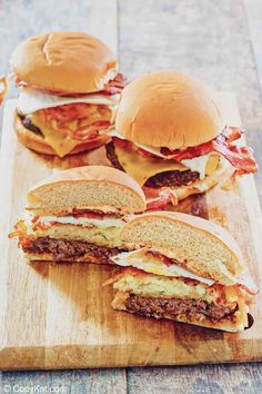 three cheeseburgers on a cutting board with bacon and melted cheese in the middle