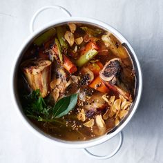 a white bowl filled with meat and vegetables on top of a table next to a spoon