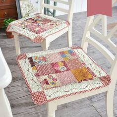 two white chairs sitting next to each other on top of a wooden floor covered in patchwork