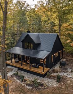 a black cabin in the woods surrounded by trees and rocks, with an open floor plan