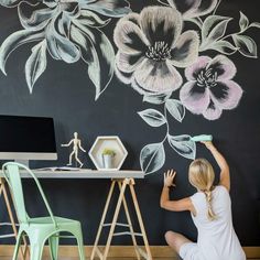 a woman sitting on the floor in front of a wall with flowers painted on it