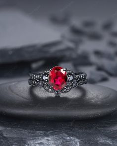 a ring with a red stone in the center on top of a black rock surface