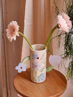 two pink flowers are in a vase on a table next to a potted plant