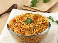 a bowl filled with rice and vegetables on top of a white napkin next to a wooden spoon