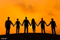 four people holding hands while standing on top of a hill with the sun in the background