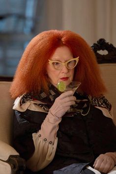 a woman with red hair and glasses holding a drink