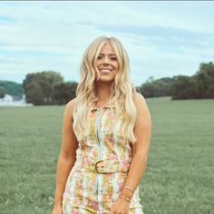 a woman standing in the grass with her hand on her hip and smiling at the camera