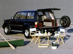 a black suv parked in front of a building next to a table with chairs on it