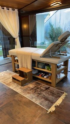 a bed sitting on top of a wooden table next to a glass window with white curtains