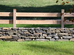 a wooden bench sitting next to a stone wall in the middle of a grass field