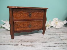 a wooden dresser with two drawers and flowers on the floor in front of blue wall