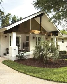 a white house with black shutters on the front porch and covered in grass, trees and shrubs