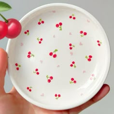 a hand holding a small bowl with cherries on it