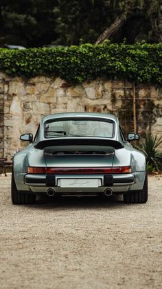 a grey porsche parked in front of a stone wall