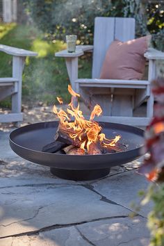 a fire pit sitting on top of a stone patio next to chairs and trees in the background