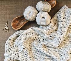 a crocheted blanket and two balls of yarn next to a pair of scissors