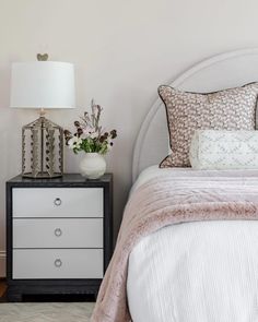 a white bed sitting next to a night stand with two lamps on top of it