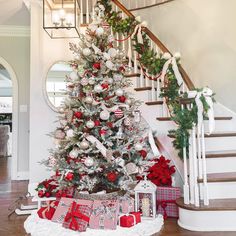 a decorated christmas tree with presents under the banister and stairs in a foyer area