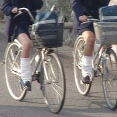 two people riding bikes with baskets on the front and back wheels, both wearing socks