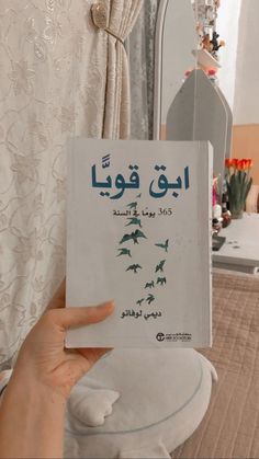 a person holding up a book in front of a mirror with arabic writing on it