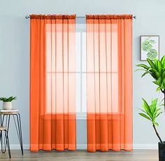 an orange curtain hanging on the side of a window next to a potted plant