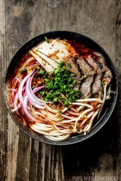 a bowl filled with meat and vegetables on top of a wooden table