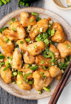 a plate full of fried chicken with green onions and chopsticks next to it