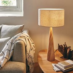 a wooden table with a lamp on it next to a book and a couch in front of a window