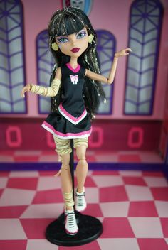 a doll is standing on a checkered floor in front of a pink and purple wall