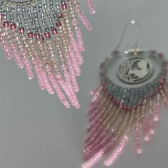 two pink and silver beaded earrings on a white surface with beads hanging from them