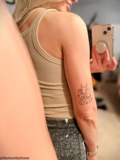 a woman with a flower tattoo on her arm taking a selfie in the mirror