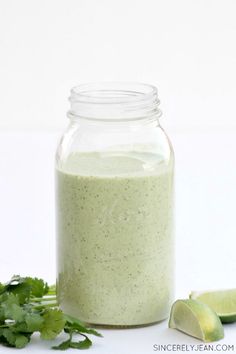 a jar filled with green liquid next to limes and cilantro on the side