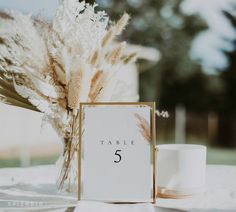 the table numbers are placed next to a vase with dry grass in it and a coffee mug