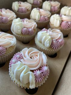 cupcakes with white and pink frosting sitting in a box on a table