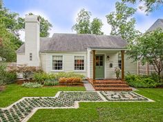 a small white house in the middle of a green yard with steps leading up to it's front door