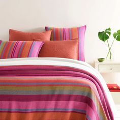 a bed with pink, orange and green striped bedspread on top of it