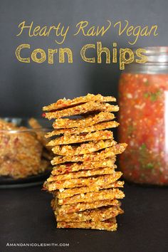 hearty raw vegan corn chips stacked on top of each other with a jar of salsa in the background