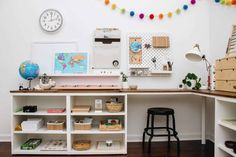 a desk with lots of books and other items on top of it next to a wall clock