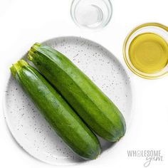 two cucumbers on a white plate next to some olive oil