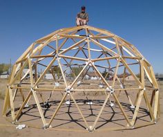 a man sitting on top of a wooden structure in the middle of a dirt field