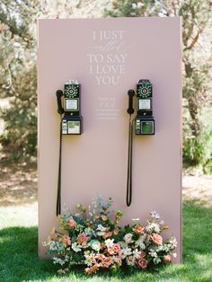 two old fashioned telephones are on display in the grass with flowers and greenery