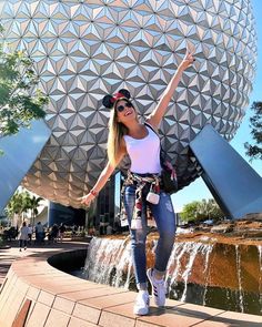 a woman is posing in front of the spaceship dome at disney world with her arms up