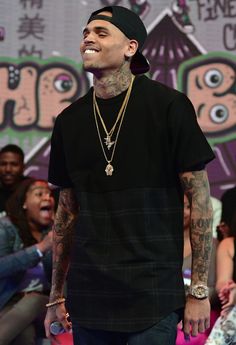 a man standing in front of a crowd wearing a black shirt and green pants with tattoos on his chest