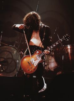 a woman with long hair playing an electric guitar in front of a microphone and drums