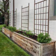 a wooden planter filled with lots of plants next to a white wall and green grass