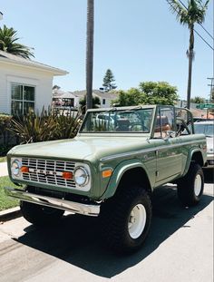 an old green pick up truck parked on the side of the road in front of a house