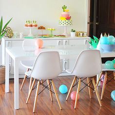 a dining room table with white chairs and colorful balloons on the floor next to it