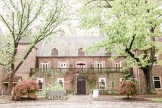 an old brick building with trees in front of it and a red umbrella over the door