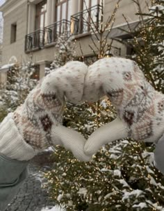 a person holding up a knitted heart in front of a tree with snow on it