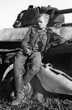 black and white photograph of a man sitting on top of a car in front of a tank